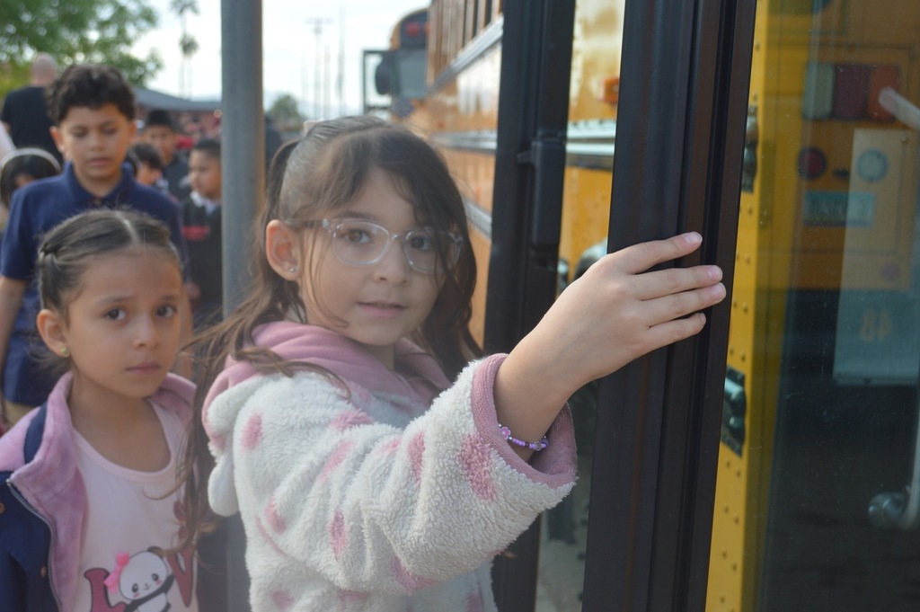 Students walking onto a school bus, two elementary students looking at the camera as they get onto the school bus