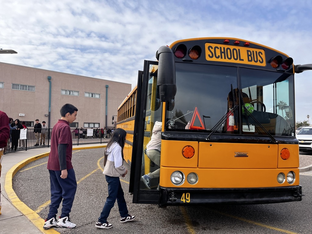 Students outdoors of their school building while they line up and get on the school bus in their school parking lot