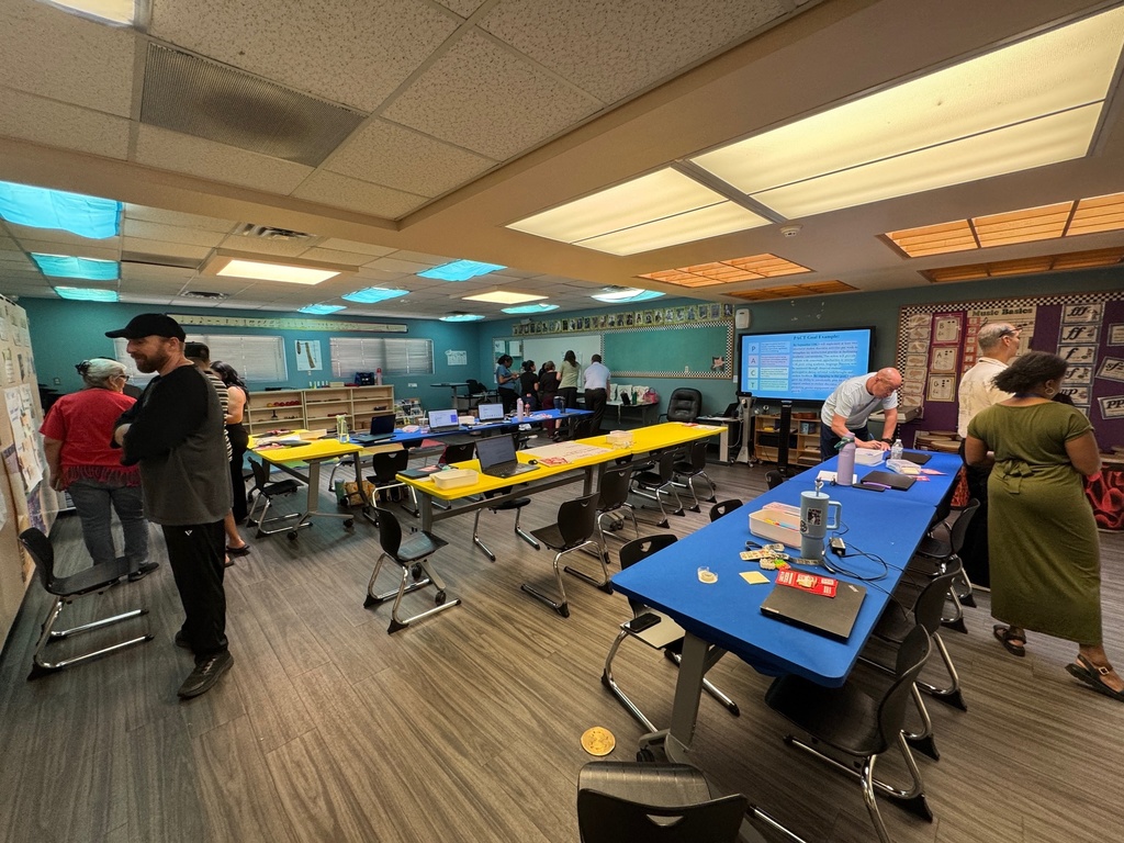 A group of people gathered around a table in a classroom, engaged in discussion and collaboration.