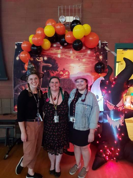 3 teachers pose in front of a fall/Halloween decorated backdrop
