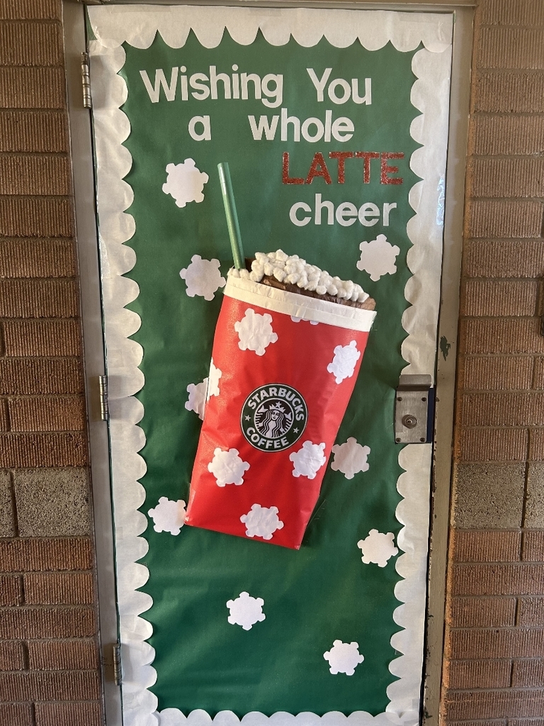 A door covered in bright green paper with white scalloped borders. The text is written in white and red glitter, reading, "Wishing You a whole LATTE cheer." A large, red and white polka-dot Starbucks-style coffee cup with a green straw and whipped cream topping is affixed to the center. Small white snowflake/cloud cutouts surround the cup.
