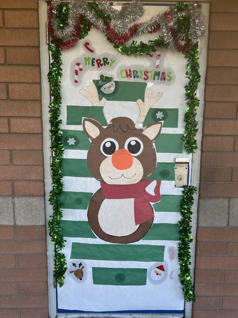 A door decorated with alternating horizontal stripes of green and white paper. A large, cartoon reindeer with a red scarf and big eyes is centered on the door. The top of the door is framed with red and green tinsel, and the words "MERRY CHRISTMAS" are written above the reindeer's head, along with small candy cane cutouts.