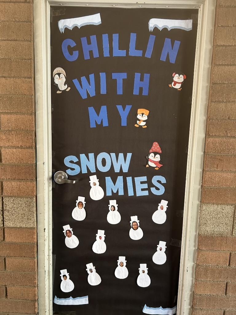 A black door covered with blue and white lettering that reads "CHILLIN WITH MY SNOWMIES." Several small cartoon penguins are scattered around the text. Below the text are twelve white paper snowman cutouts, each with a small photograph of a person's face inside the head area.