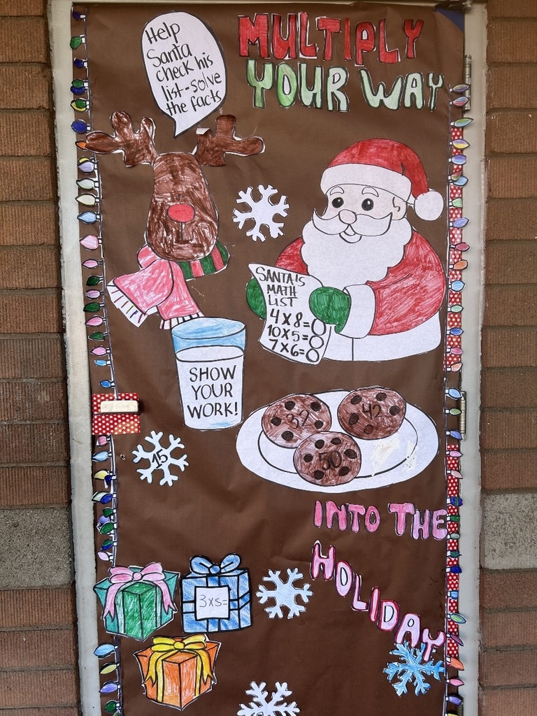 A door covered in brown paper with drawings and text celebrating the holidays and multiplication. The title reads "MULTIPLY YOUR WAY INTO THE HOLIDAY." Drawings include Santa holding a list of multiplication problems, a reindeer, a glass of milk, a plate of chocolate chip cookies, and wrapped gifts. Strings of paper Christmas lights frame the edge of the door.