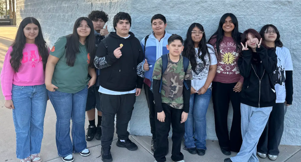 Students line up posing for a picture against a white wall