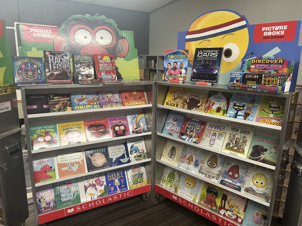 The "Picture Books" section featuring colorful covers. Titles include Grumpy Monkey, The Bad Seed, The Good Egg, and Pete the Cat. Large cardboard cutouts of a monkey and a yellow smiley face decorate the top.