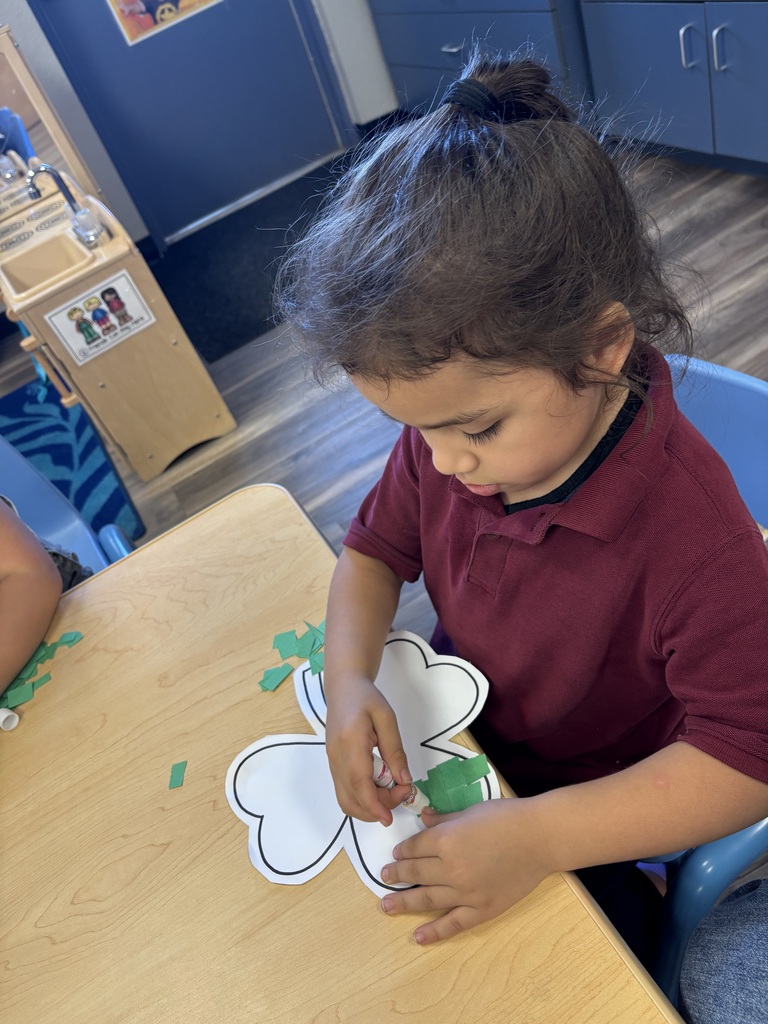 Girl gluing pieces of green paper to outline of a shamrock