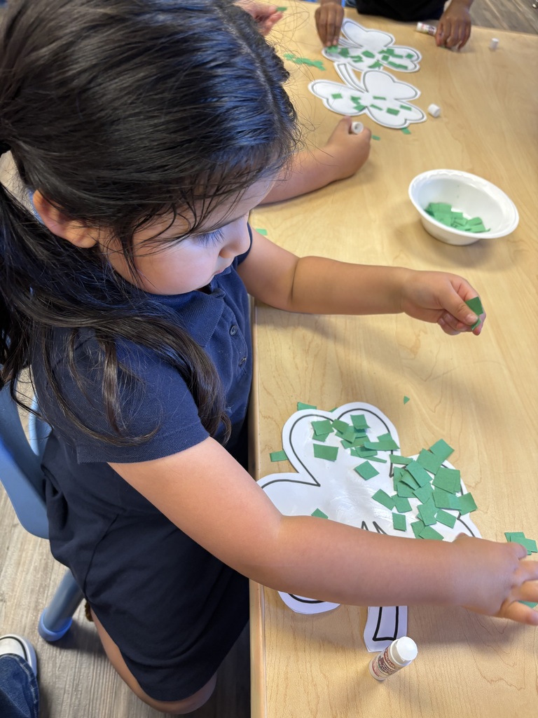 Girl gluing pieces of green paper to outline of a shamrock