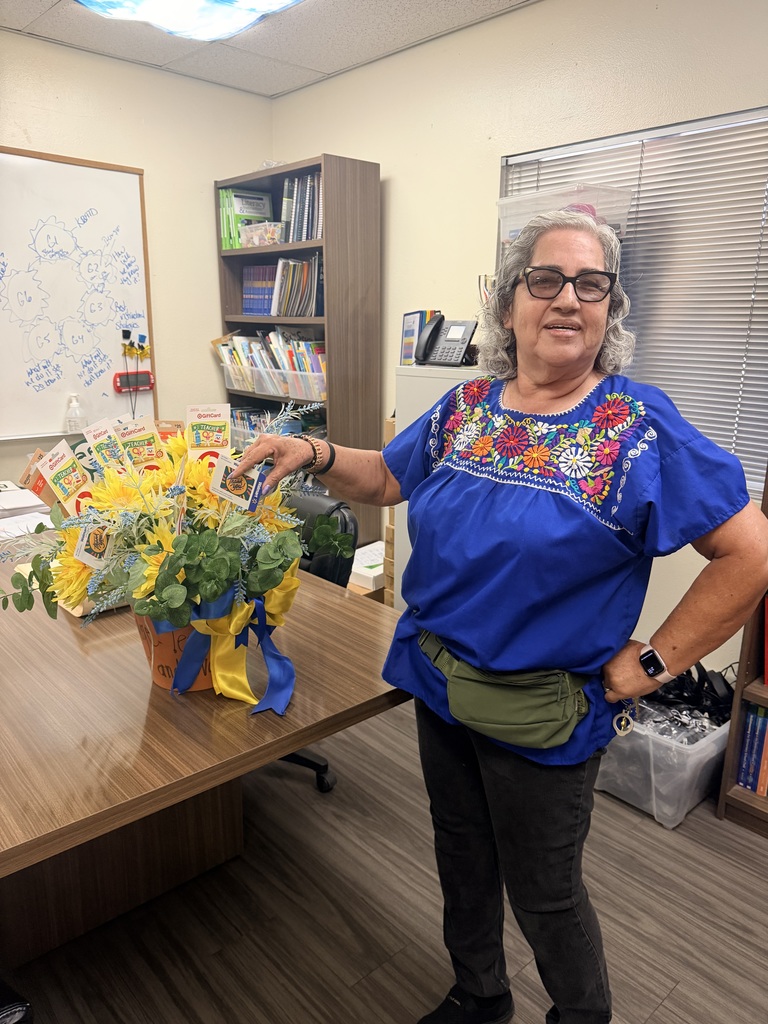 Woman in a blue embroidered blouse pointing to a gift card in the bouquet.