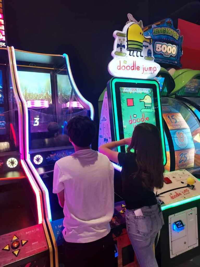Two kids play on arcade machines
