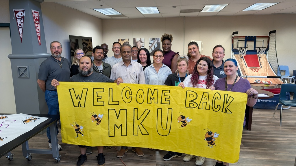 Staff pose for a picture holding a sign that says "welcome back MKU"