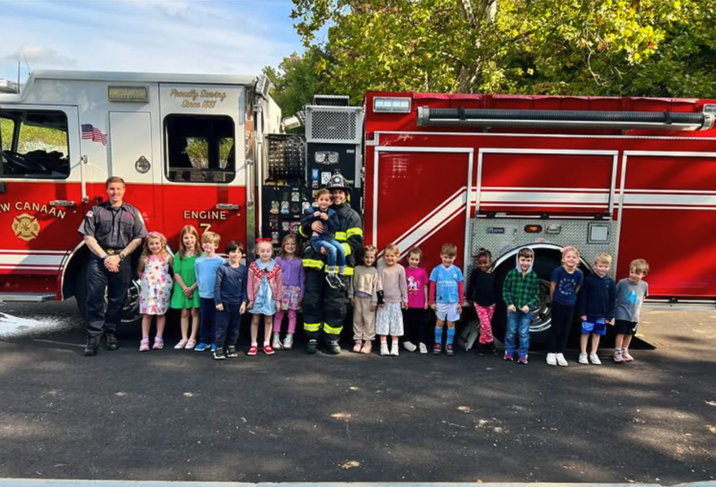 Children standing in front of a fire truck with a fire fighter