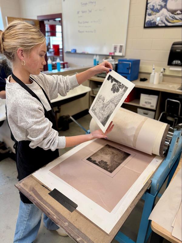student checking artwork in printing press while exploring curisoity