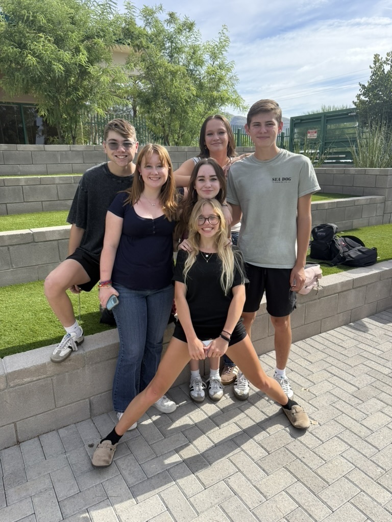Six individuals pose for a photo on a brick walkway with a grassy area and stone steps behind them.