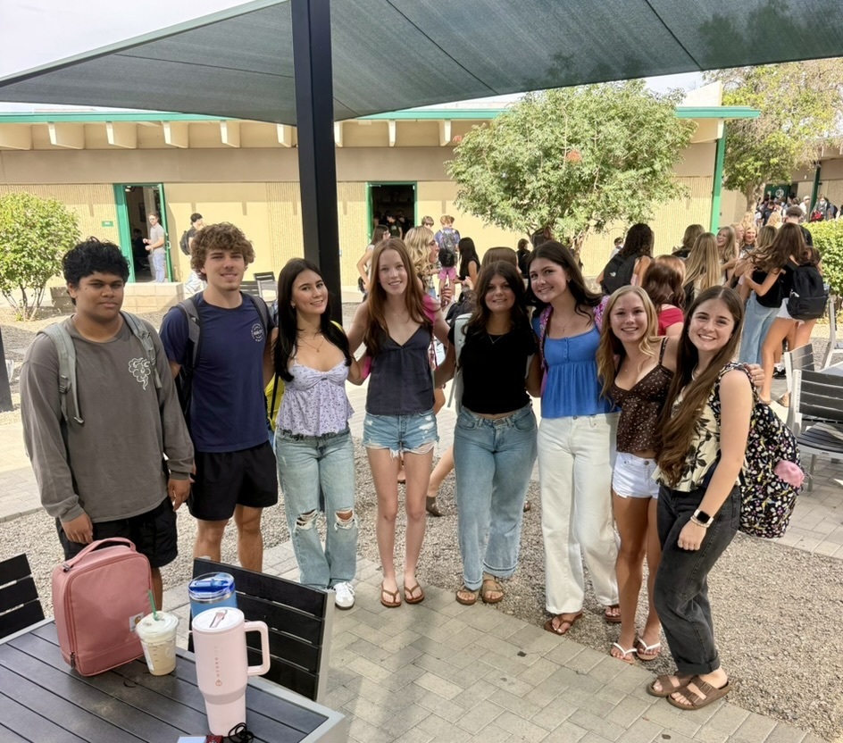 A group of young people wearing casual clothing and standing outside in a courtyard with tables.