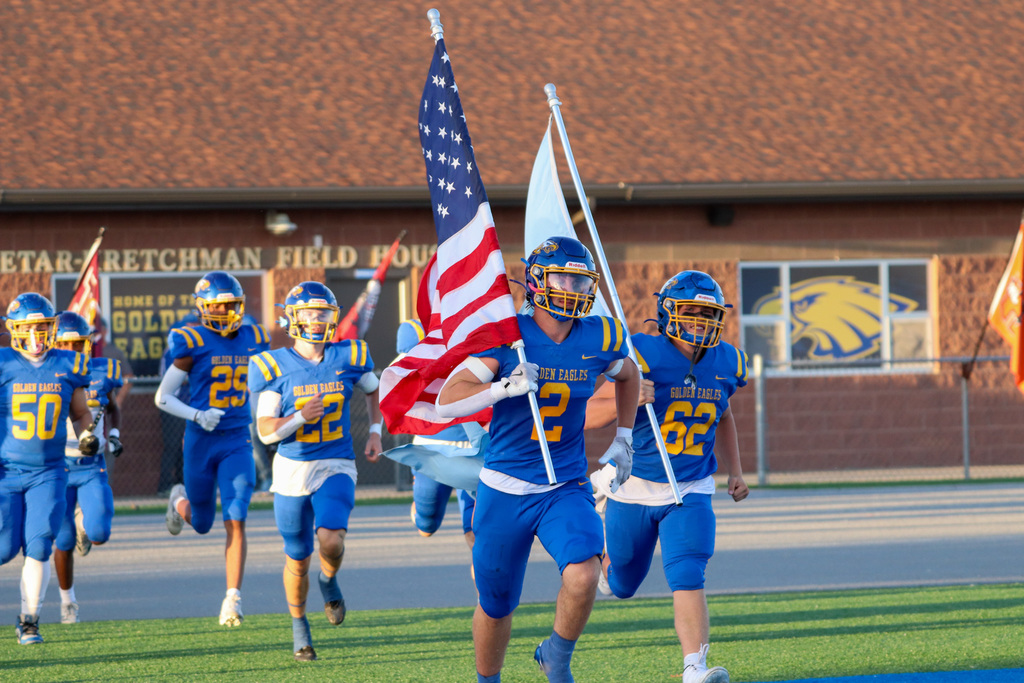 Football players carrying the US flag at homecoming