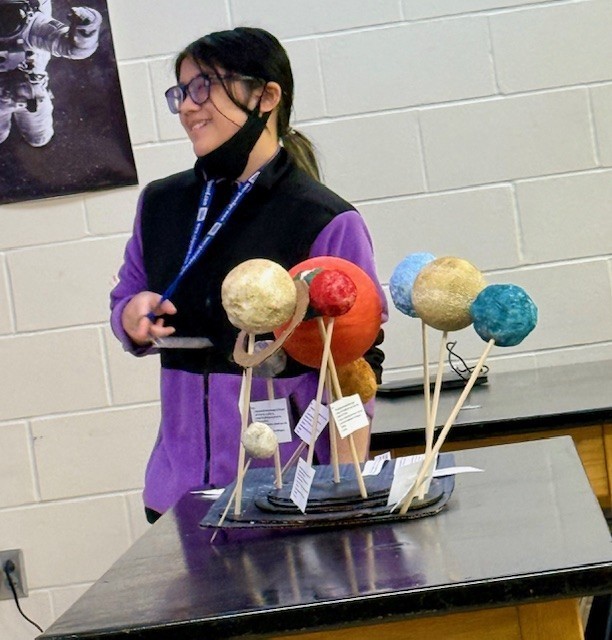 A student presents her scale model, explaining orbital distances and proportional sizing.
