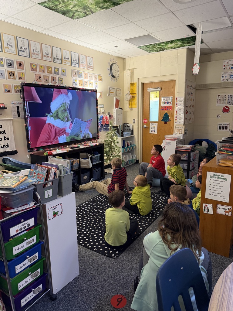 A group of students in a classroom watch the live-action Grinch read "How the Grinch Stole Christmas". 