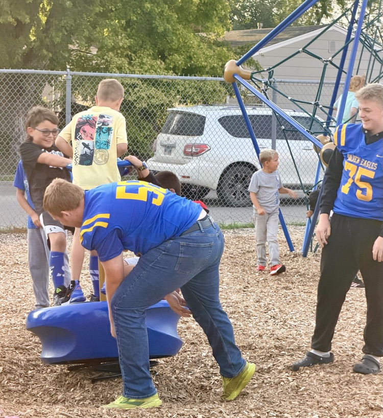 High school football players on playground with elementary students.