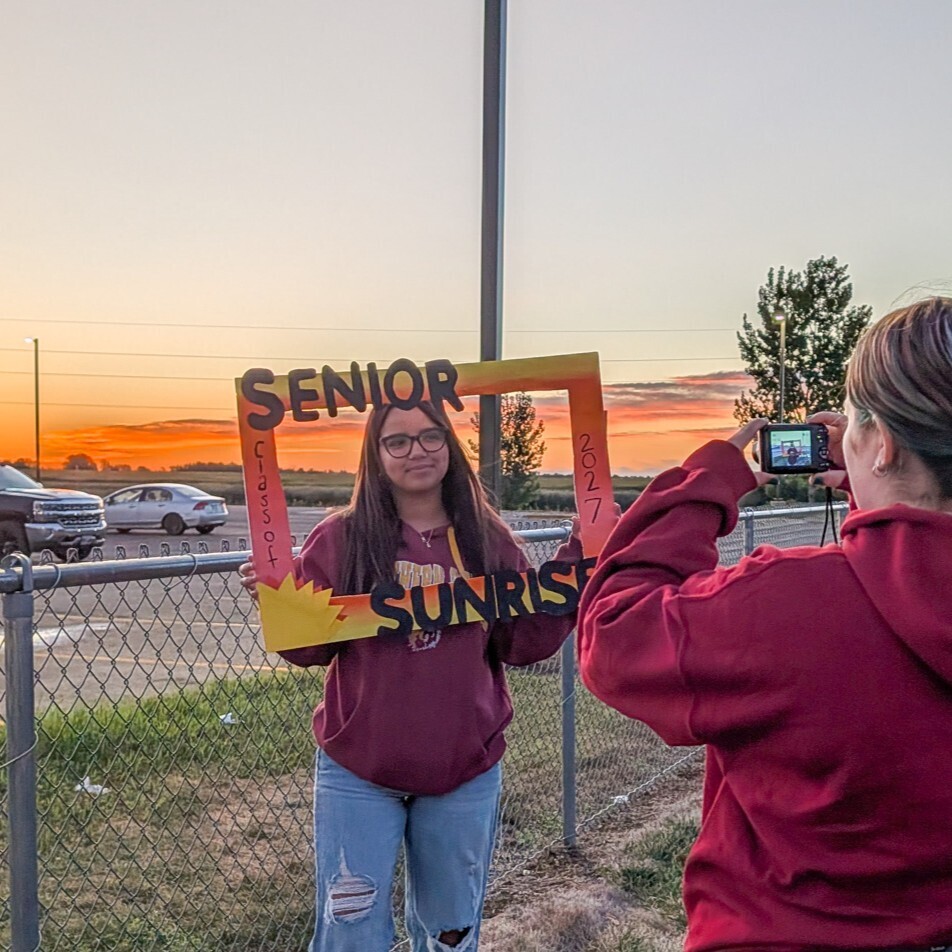 CHS senior posing with a Senior Sunrise frame with the sunrise in the background
