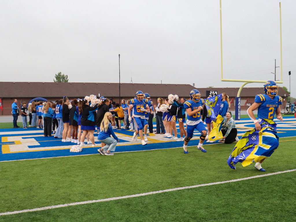 CHS football players running through a homecoming banner held by students
