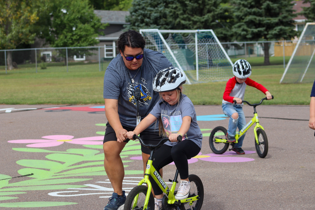 A C.C. Lee student riding a Strider bike during gym class with the help of Ms. Hansen