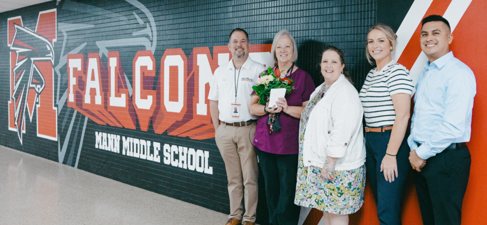 A photo of Dr. Kuhn, Nurse Mary Vermillion, Director of Health Services Angela Valentine, and representatives from First Financial Bank in front of a Mann Middle School mural