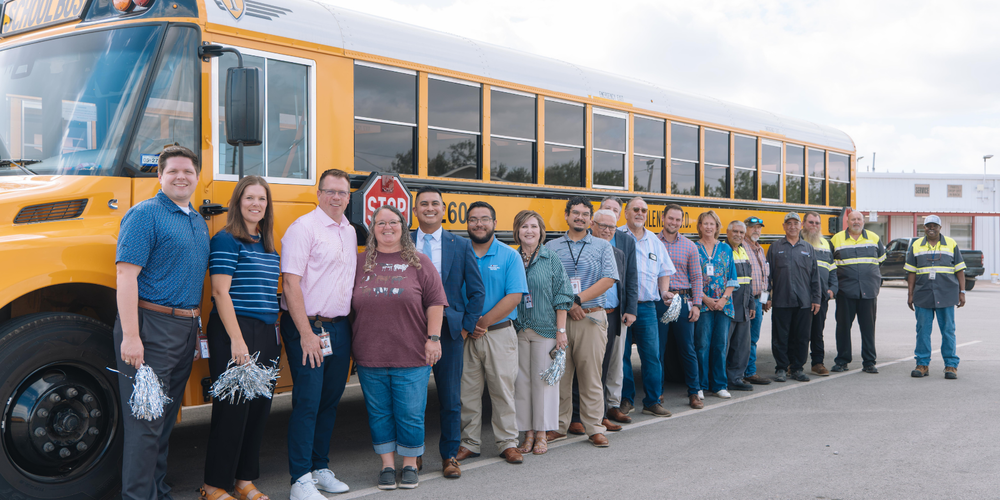 A photo of Misty Miller, transportation team members, and district leadership in front of a school bus