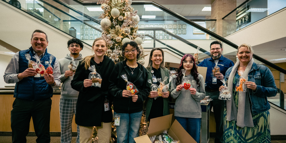 A photo of CHS students and staff with Hendrick staff holding the donations in front of a Christmas tree