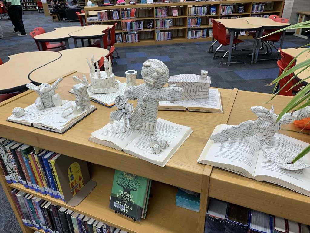 Book shelf in library with art displays from students made out of old books.