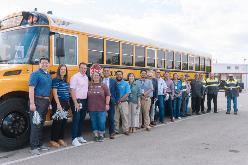 A photo of Misty Miller, the transportation team, and district leadership team members in front of a school bus