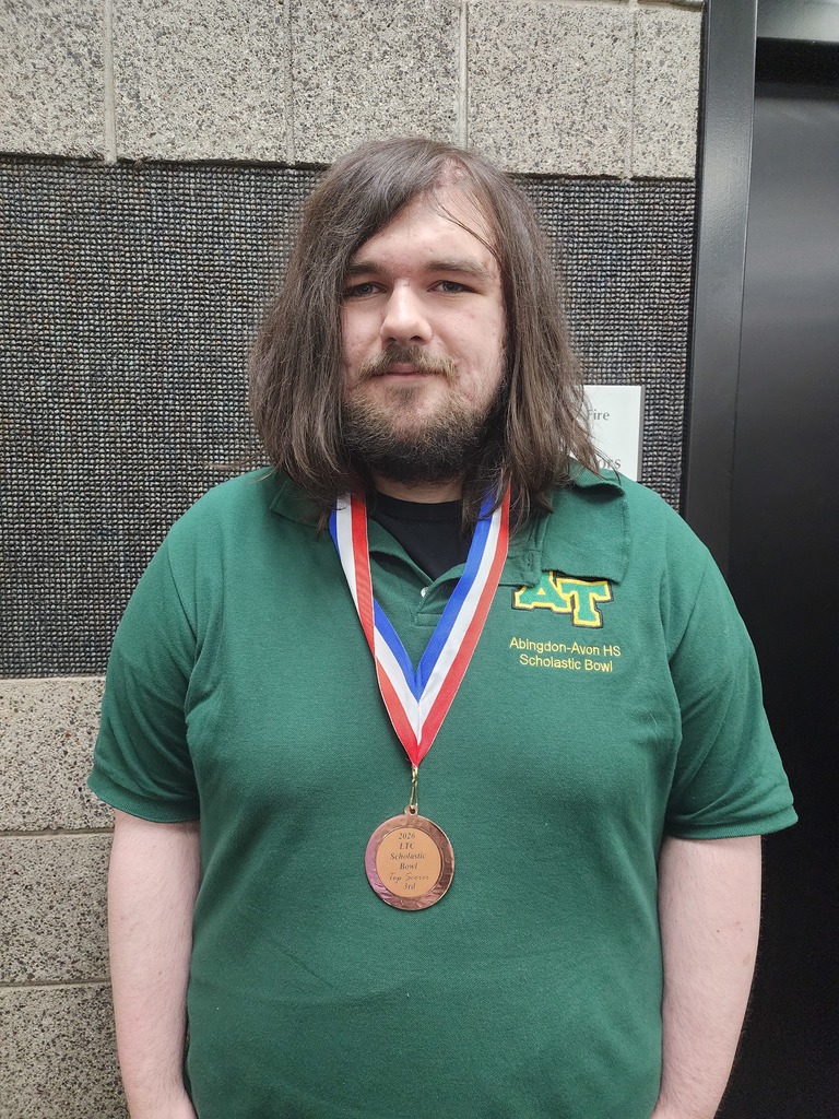 A young man with long brown hair wearing a green polo shirt and a medal around his neck.