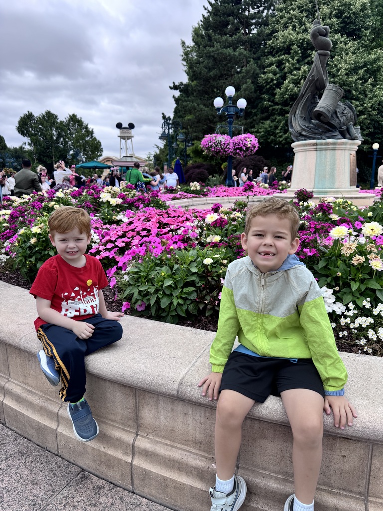 Leo and his brother Charlie sit in front of a fountain with flowers in Paris