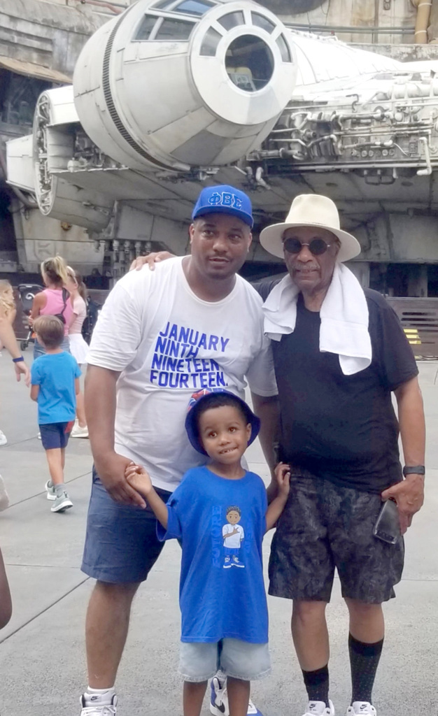 AJ holds hands with his dad and grandfather in front of the Millennium Falcon ride at Disney World Hollywood Studios in Florida.