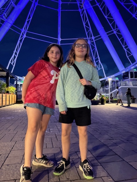Elena and Audra stand inside of the Biodome where the arched ceiling, lighted with blue lights, can be seen