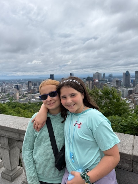 Audra and Elena stand in front of a stone wall overlooking the city of Montreal, Canada