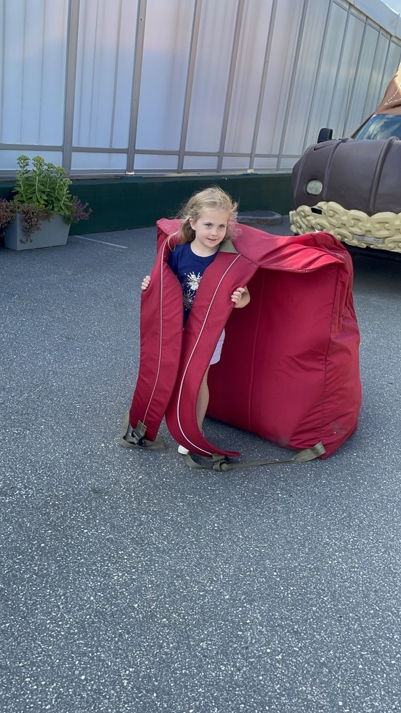 Elizabeth is wearing a very over-sized red bookbag, standing in a parking area
