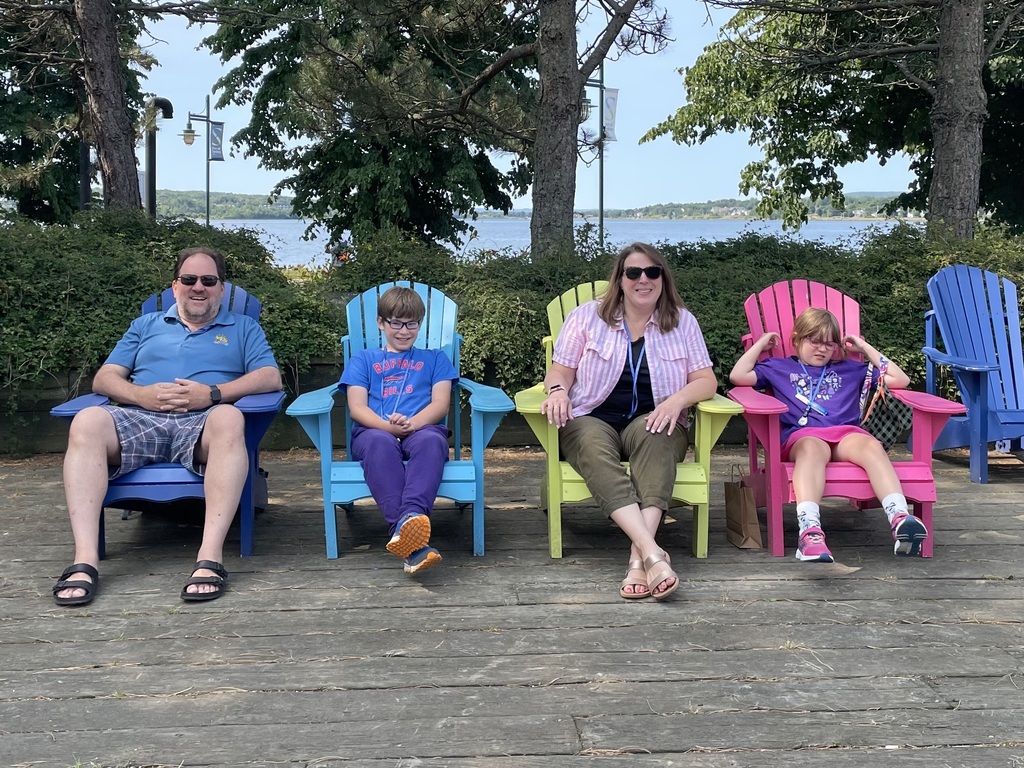 Chase and Abby sit on colorful Adirondack chairs with their mom and dad in front of a body of water and greenery