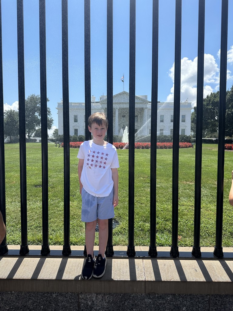 Robbie  stands in front of a black fence with the White House in the background