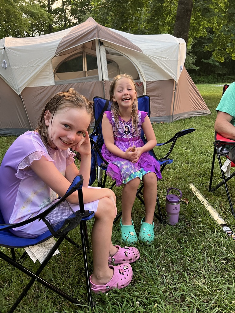 Sheileen and Annaleia are sitting in camping chairs laughing with a camping tent in the background
