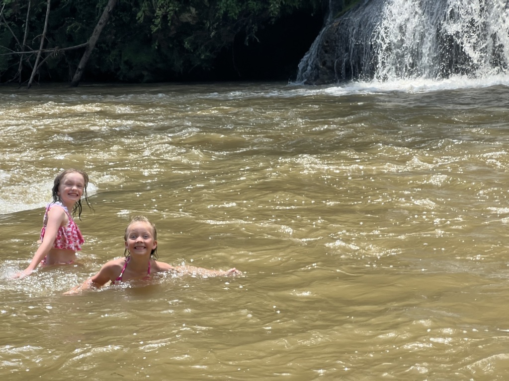 Sheileen and Annaleia are swimming in water with a waterfall right behind them