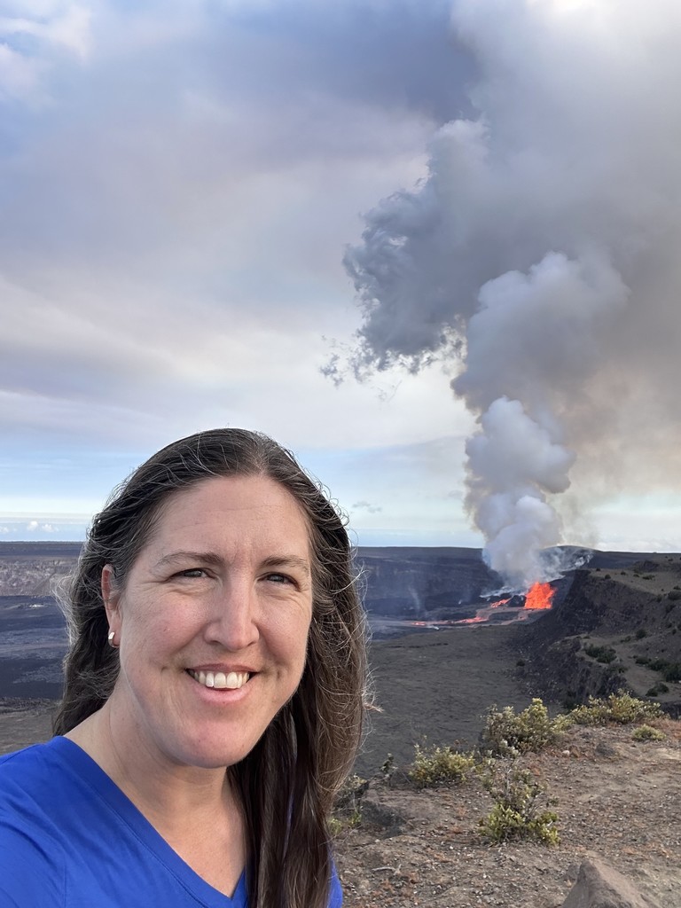 Mrs. Bocian standing with Kilauea volcano erupting in the background