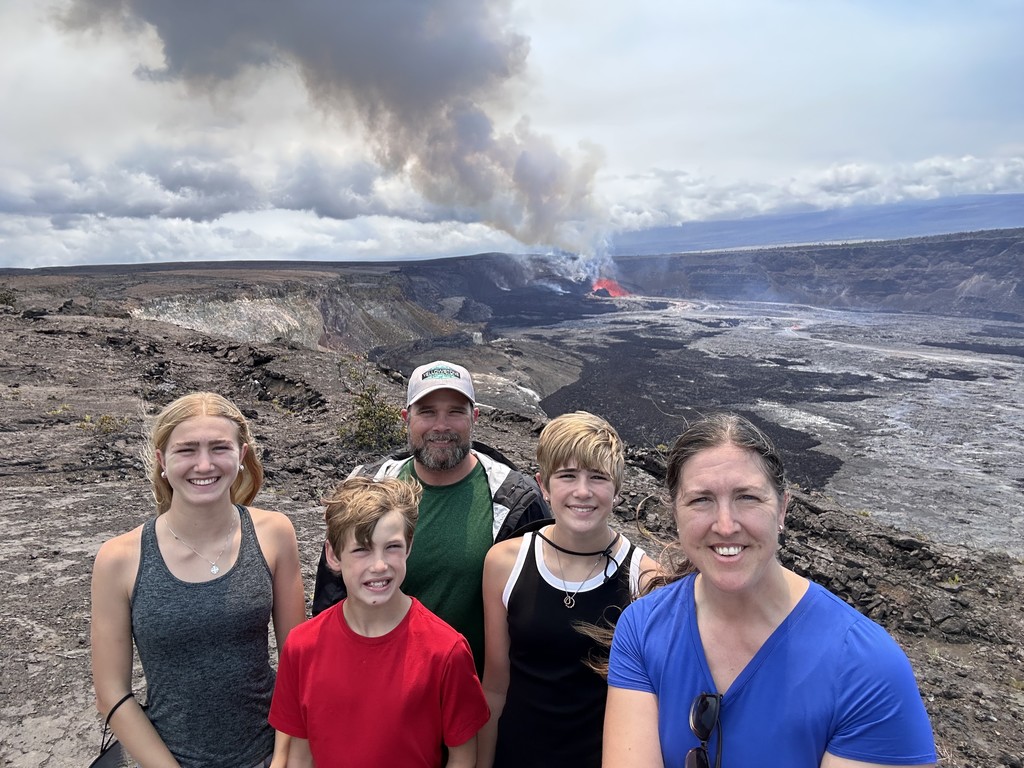 Mrs. Bocian and her family are standing on rocks with a steaming volcano in the background