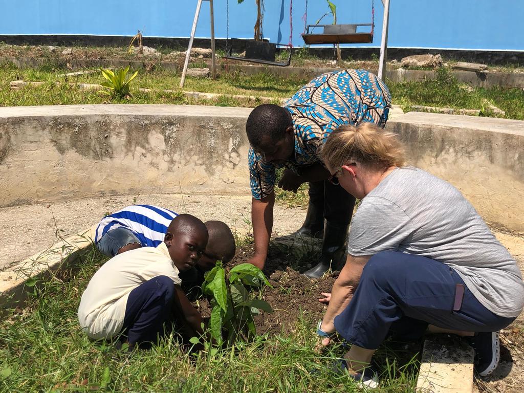 Ms. Goldberg, 2 children and another adult plant a small avocado plant in dirt