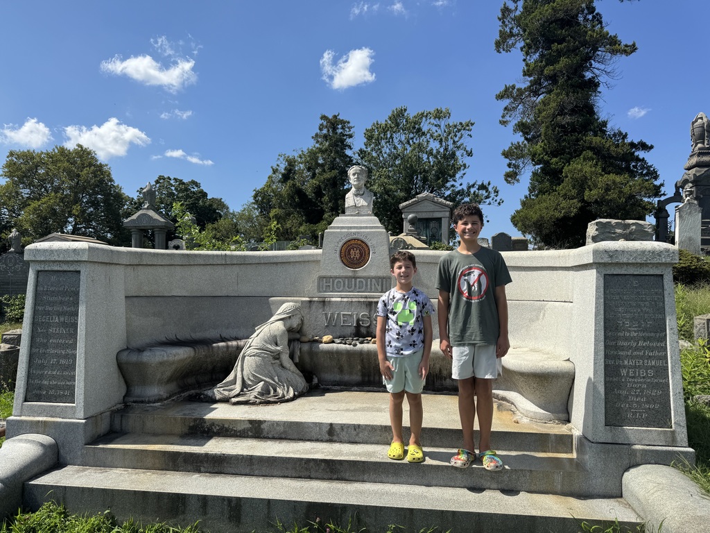 Eli and Ben stand in front of a concrete monument in a cemetery