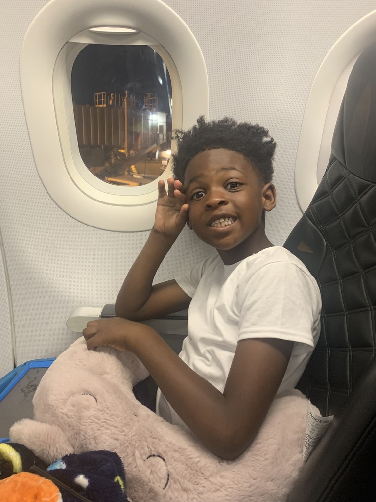 Jamarr sits in his seat next to a window on the airplane, holding a fluffy cushion for the ride