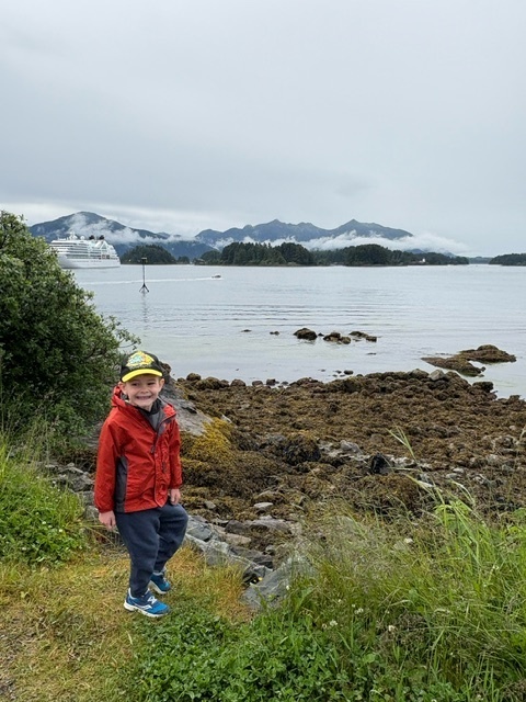 Eric stands in front of a beautiful landscape with a body of water, rocks and ice-capped mountains in the background