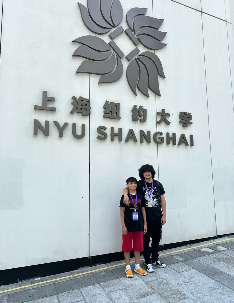 Jonathan and Walter stand in front of a white wall with the large logo "NYU Shanghai" behind them
