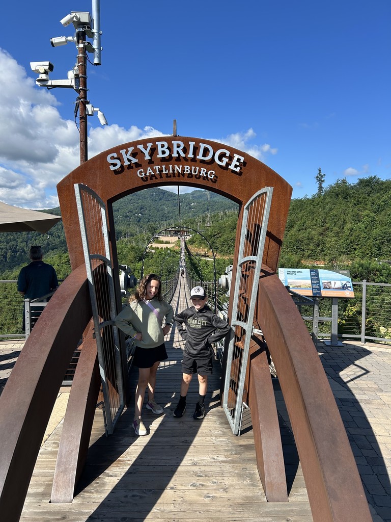 Samantha & Nathaniel stand in the entryway of a wooden sky bridge, with an arch reading "SKYBRIDGE GATLINBURG"