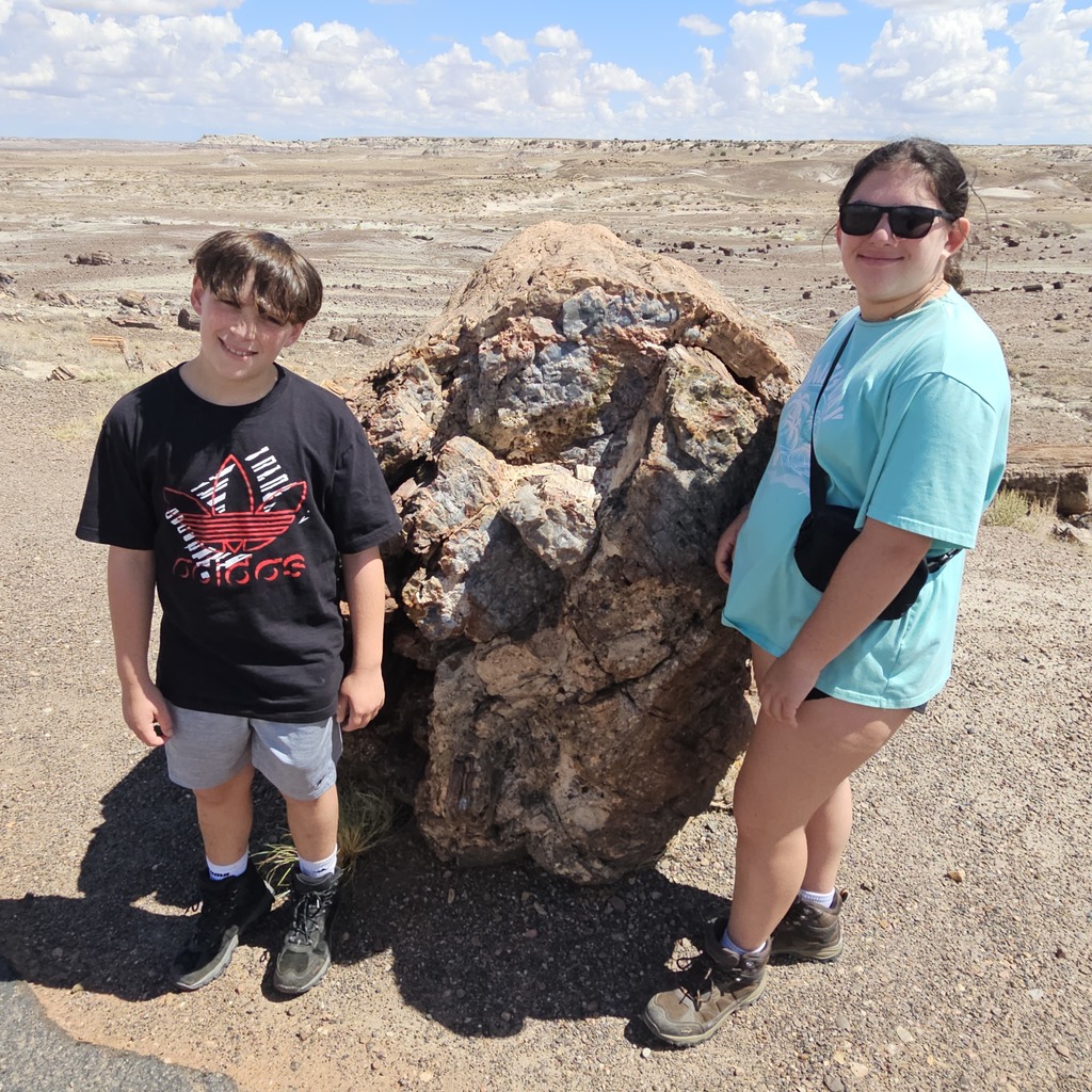 Ben and Adina  stand in a rocky desert in front of a large bolder